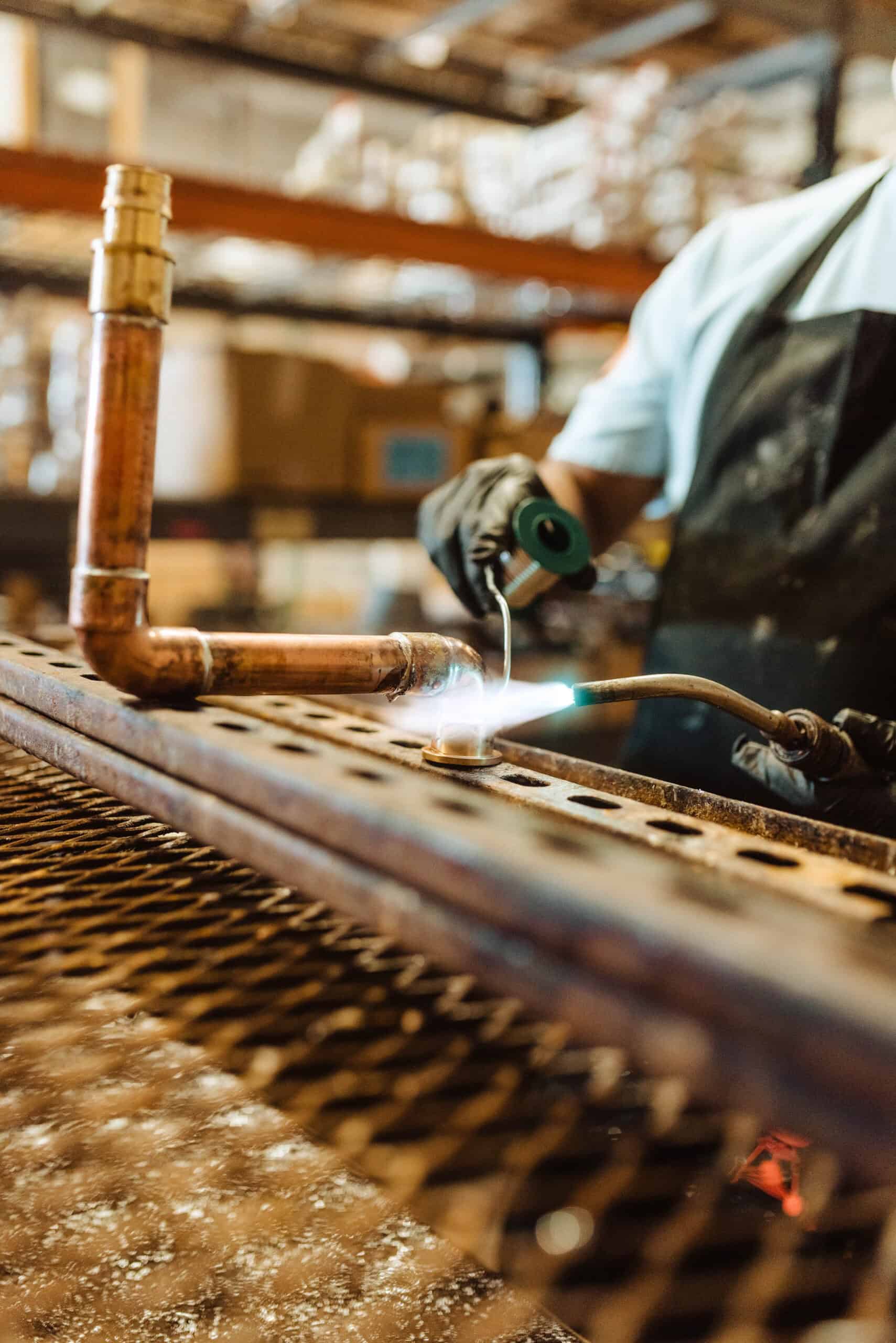 Plumber using a torch to solder a copper pipe joint on a workbench, ensuring a strong and leak-free connection.