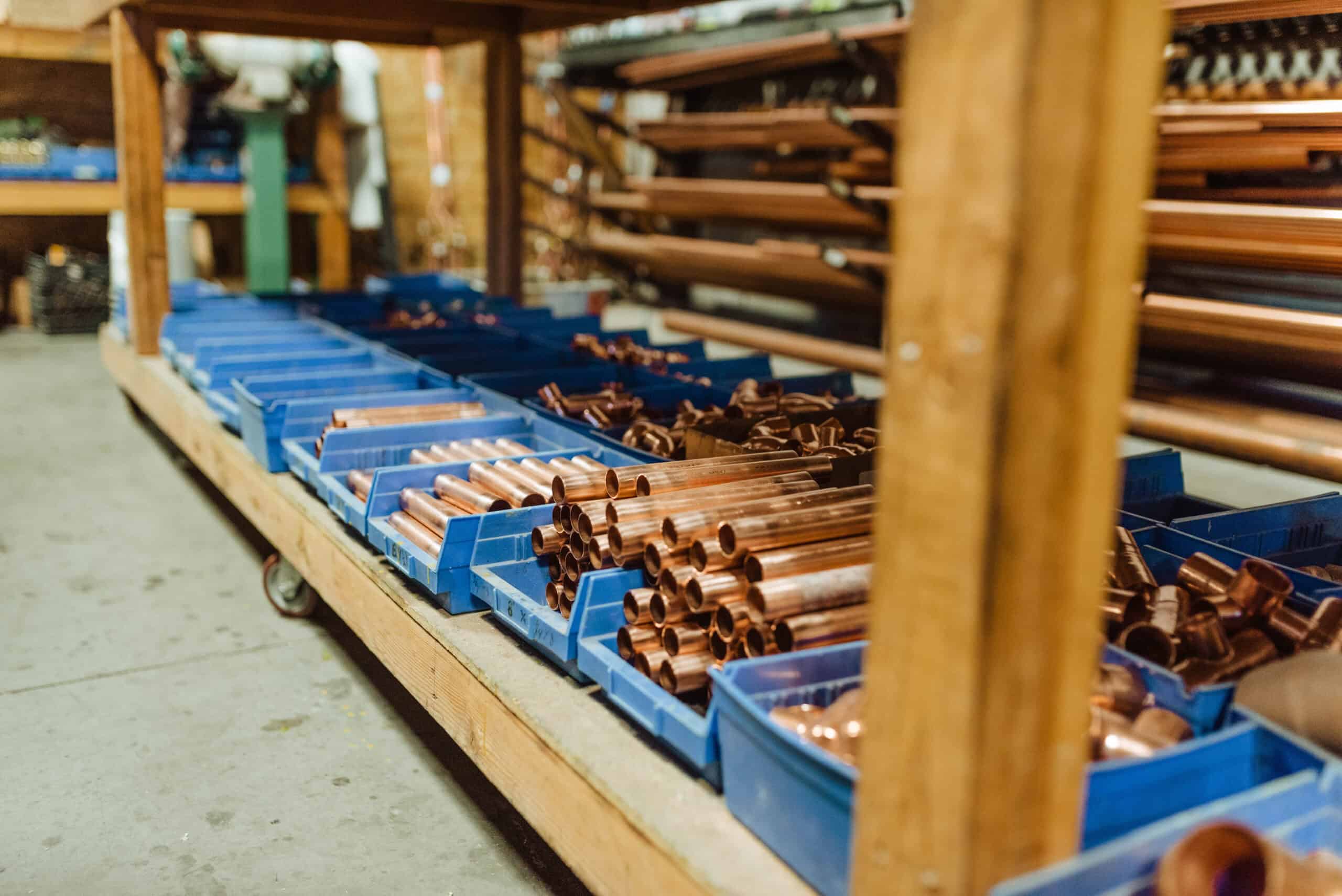 Organized copper pipes and fittings stored in labeled bins on warehouse shelving, ready for plumbing installation and job preparation.