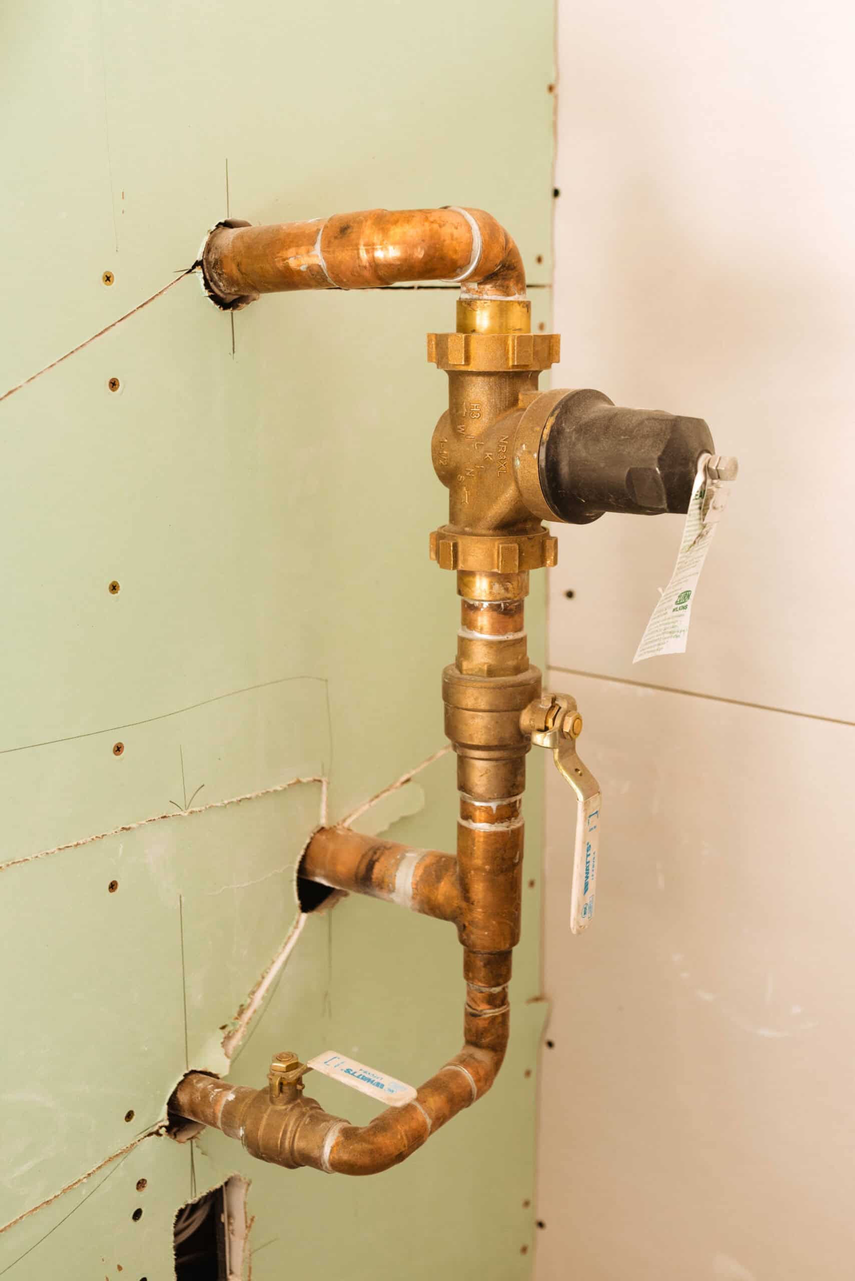 Copper plumbing assembly with valves and pressure regulator installed inside a wall, part of a residential water supply system.