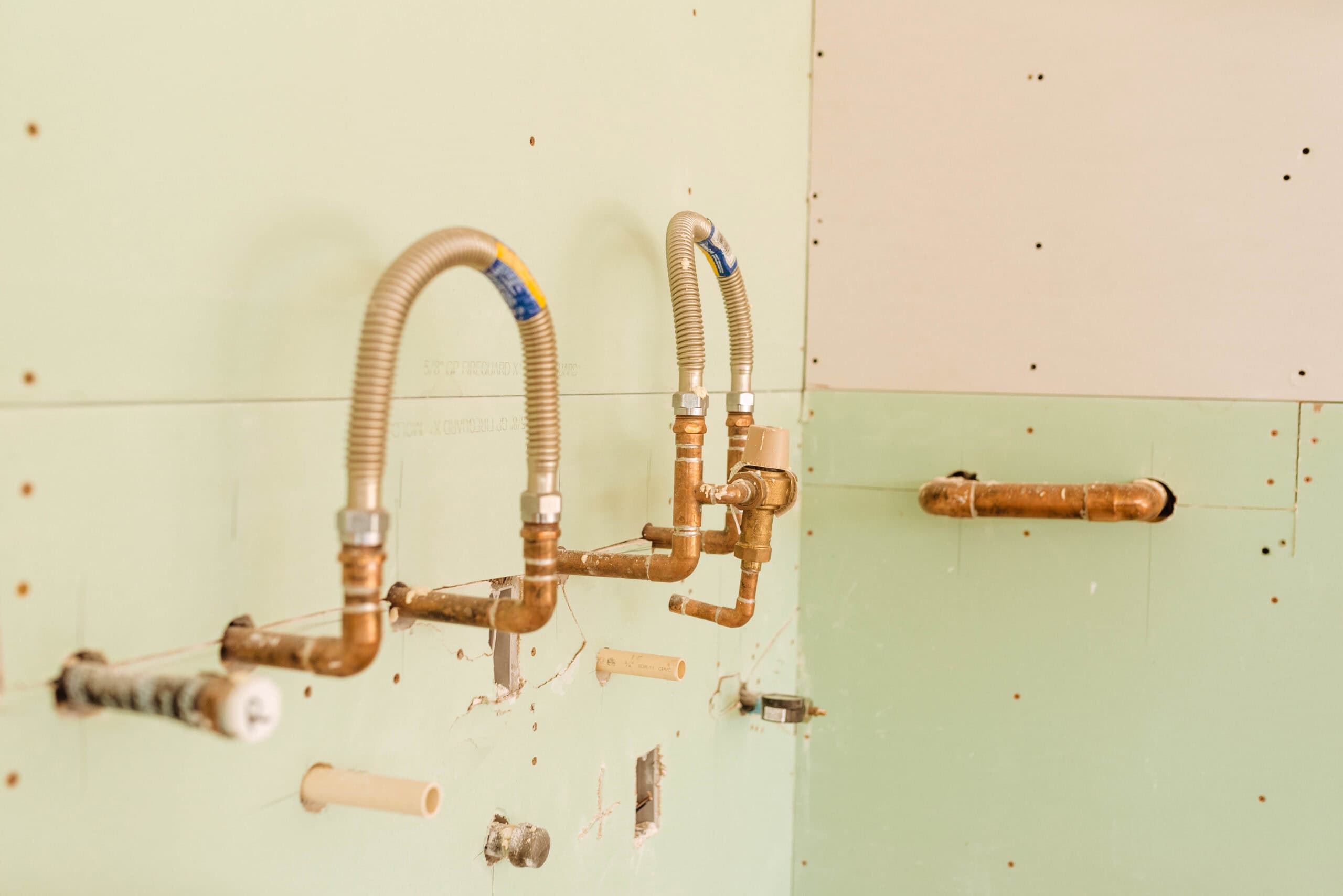 Rough-in plumbing installation with exposed copper pipes and flexible supply lines mounted inside a wall during construction.