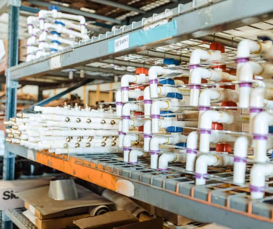 Pre-assembled plumbing manifolds and pipe fittings organized on warehouse shelving, prepared for installation and efficient job site deployment.