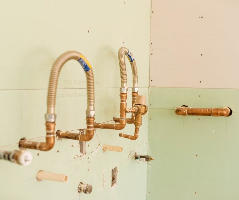 Rough-in plumbing installation with exposed copper pipes and flexible supply lines mounted inside a wall during construction.